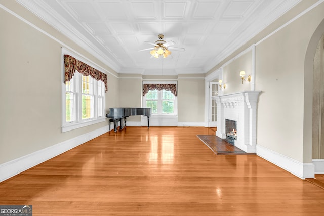living room with a ceiling fan, a warm lit fireplace, arched walkways, light wood-style floors, and an ornate ceiling