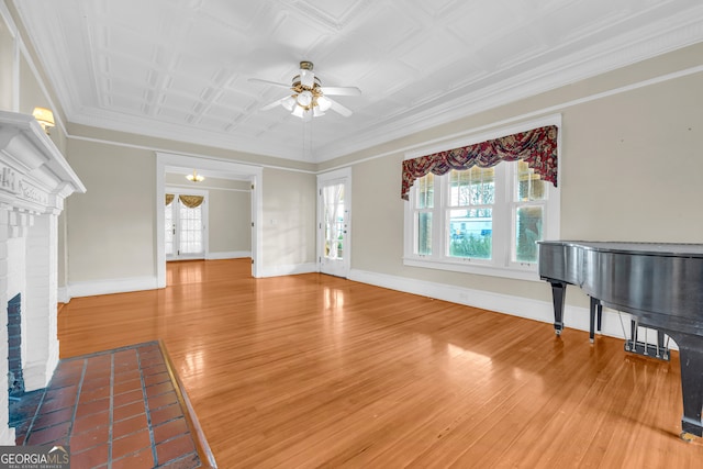unfurnished living room with ceiling fan, wood finished floors, baseboards, a brick fireplace, and crown molding