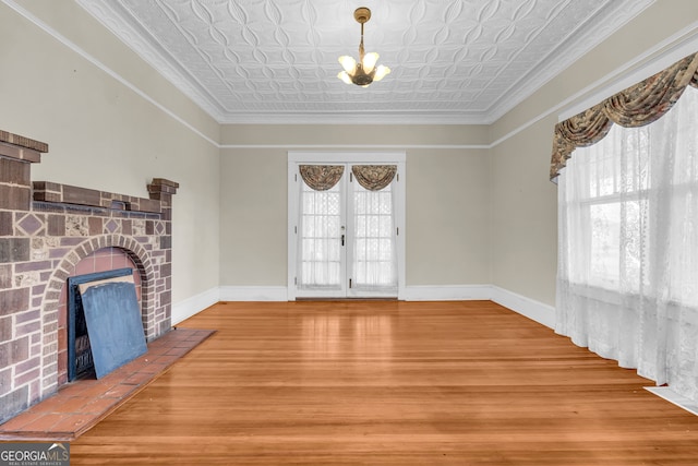 interior space with a fireplace, wood-type flooring, ornamental molding, an inviting chandelier, and french doors