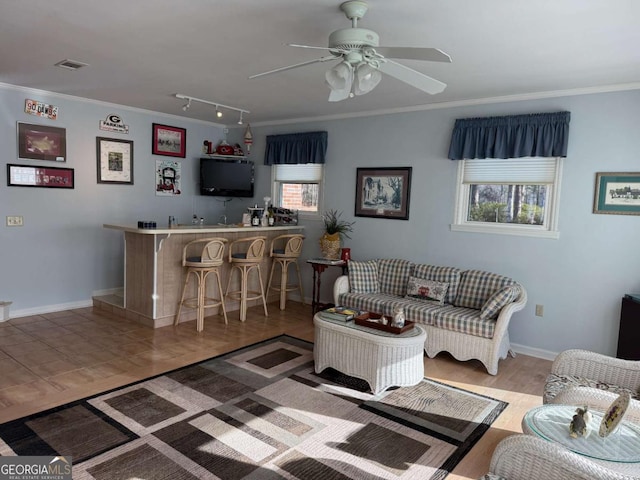 living area with ceiling fan, ornamental molding, indoor wet bar, and visible vents