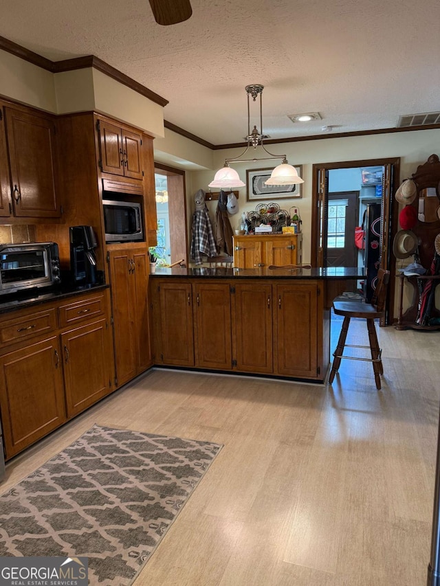 kitchen with a toaster, dark countertops, light wood-style flooring, stainless steel microwave, and ornamental molding