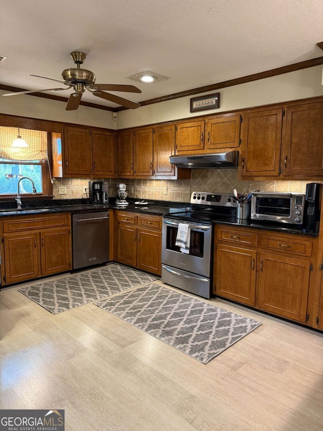 kitchen featuring a toaster, dark countertops, appliances with stainless steel finishes, under cabinet range hood, and a sink