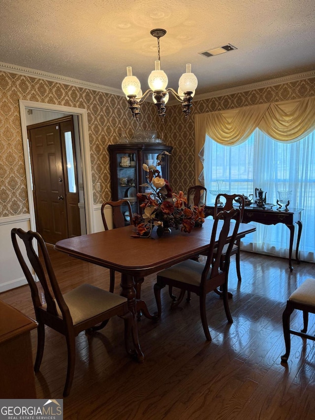 dining space with a wainscoted wall, visible vents, a notable chandelier, and wallpapered walls