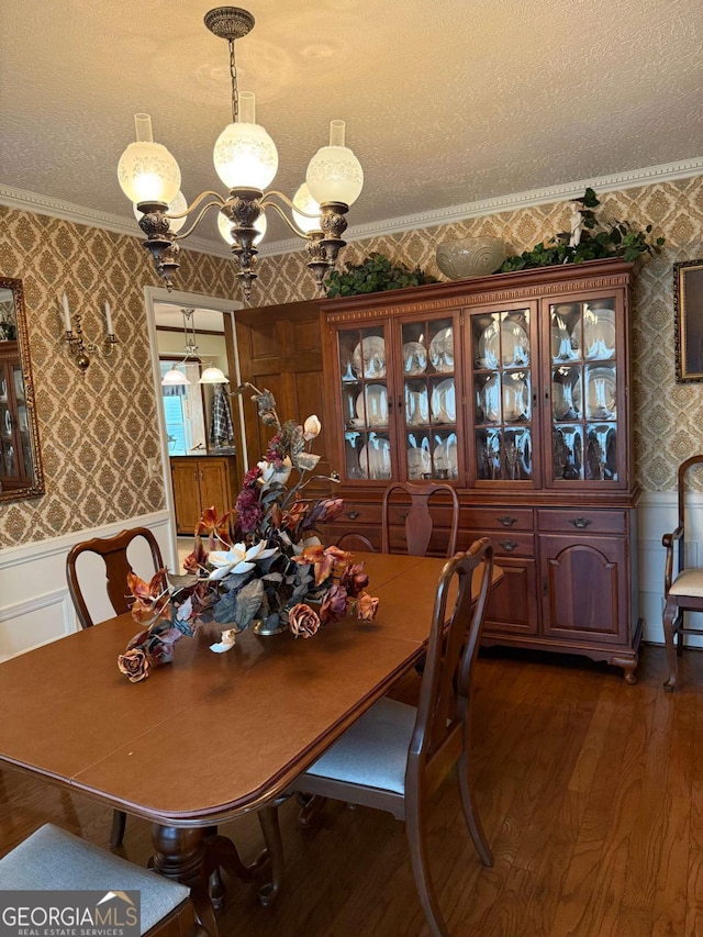 dining room with a wainscoted wall, dark wood finished floors, an inviting chandelier, a textured ceiling, and wallpapered walls