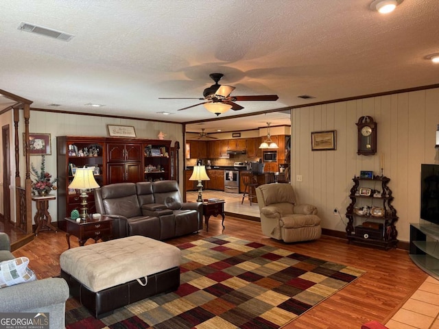 living area with ornamental molding, visible vents, and wood finished floors