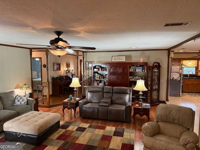 living area with a textured ceiling, wood finished floors, visible vents, and a ceiling fan