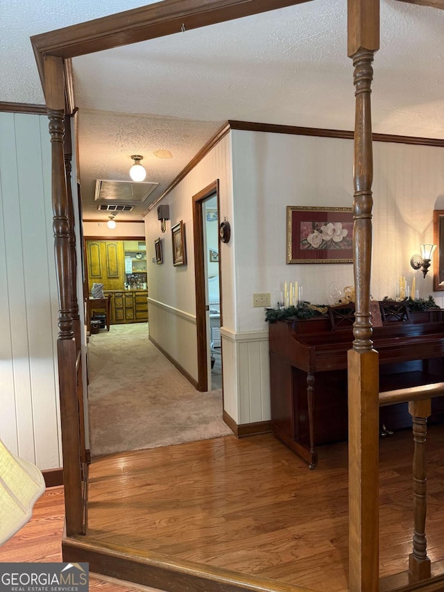 corridor with a textured ceiling, wainscoting, wood finished floors, and crown molding