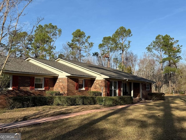 view of property exterior featuring a shingled roof, brick siding, and a lawn