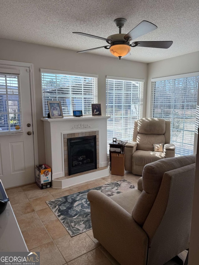 living room with ceiling fan, a textured ceiling, and a tiled fireplace