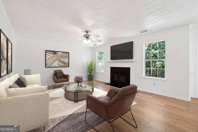 living room with ceiling fan, a textured ceiling, and light hardwood / wood-style floors