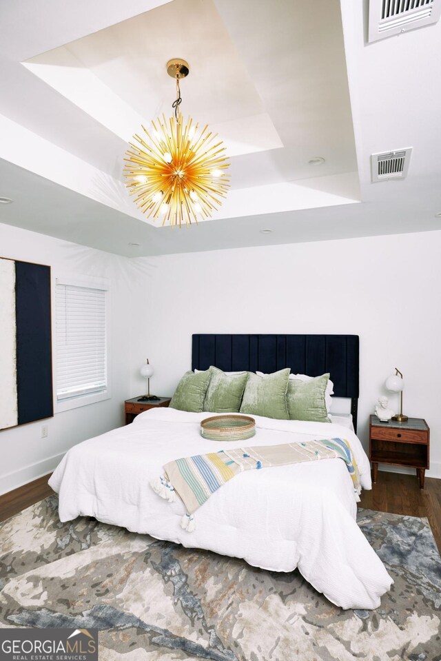 bedroom featuring wood-type flooring, a chandelier, and a tray ceiling