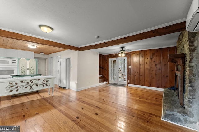 unfurnished living room featuring a stone fireplace, light wood-type flooring, ornamental molding, a wall unit AC, and beam ceiling