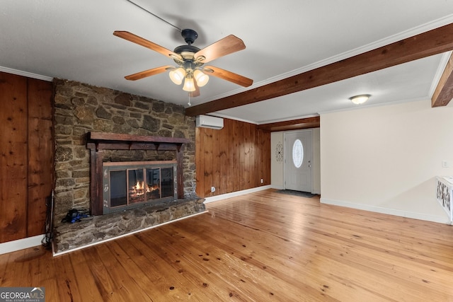 unfurnished living room with ornamental molding, a stone fireplace, light wood-type flooring, and a wall unit AC