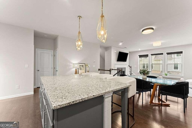 kitchen with a breakfast bar, decorative light fixtures, dark hardwood / wood-style flooring, a kitchen island, and light stone countertops