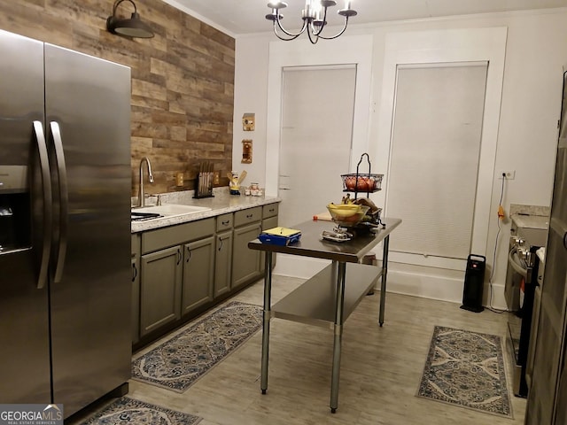 kitchen with stainless steel refrigerator with ice dispenser, sink, an inviting chandelier, ornamental molding, and wooden walls