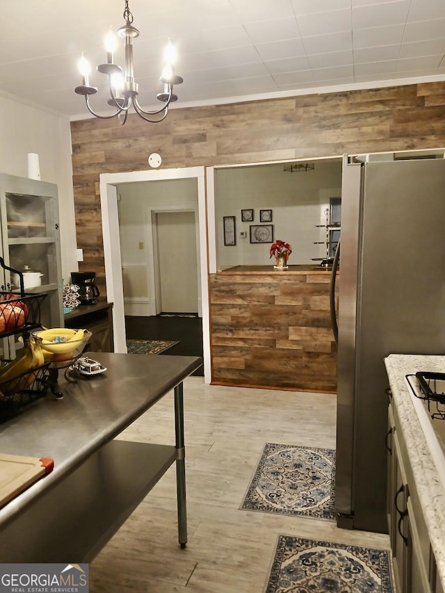 kitchen featuring pendant lighting, stainless steel fridge, light hardwood / wood-style flooring, wooden walls, and ornamental molding