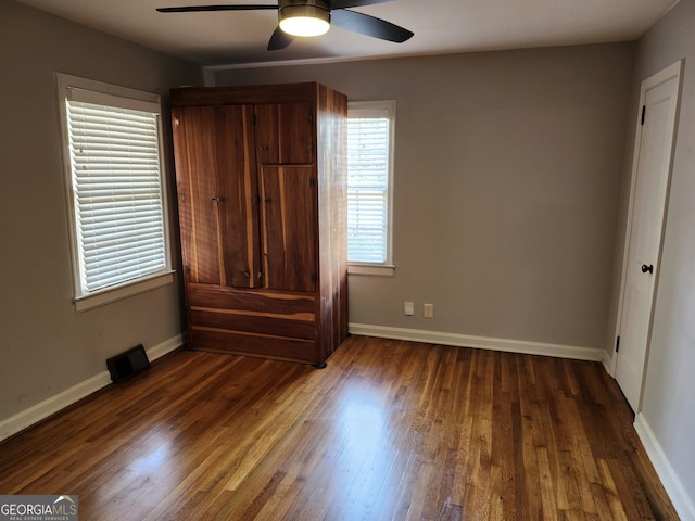 unfurnished bedroom featuring multiple windows, dark wood-type flooring, and ceiling fan