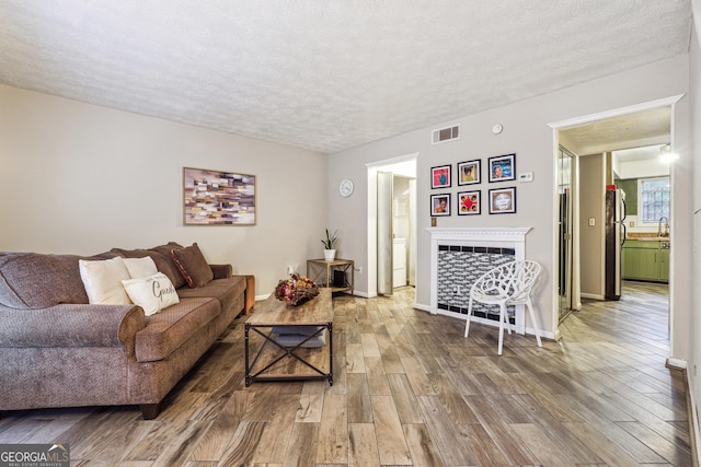 living area with baseboards, visible vents, wood finished floors, a textured ceiling, and a fireplace