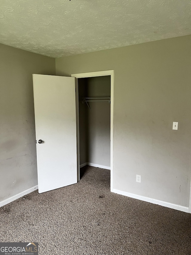 unfurnished bedroom with a textured ceiling, dark carpet, and a closet