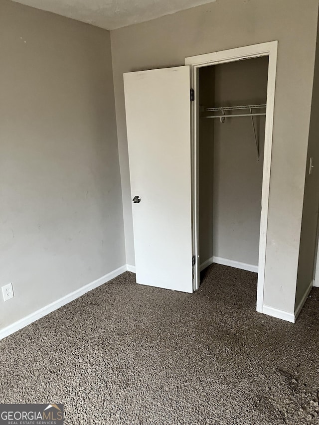 unfurnished bedroom featuring dark carpet and a closet