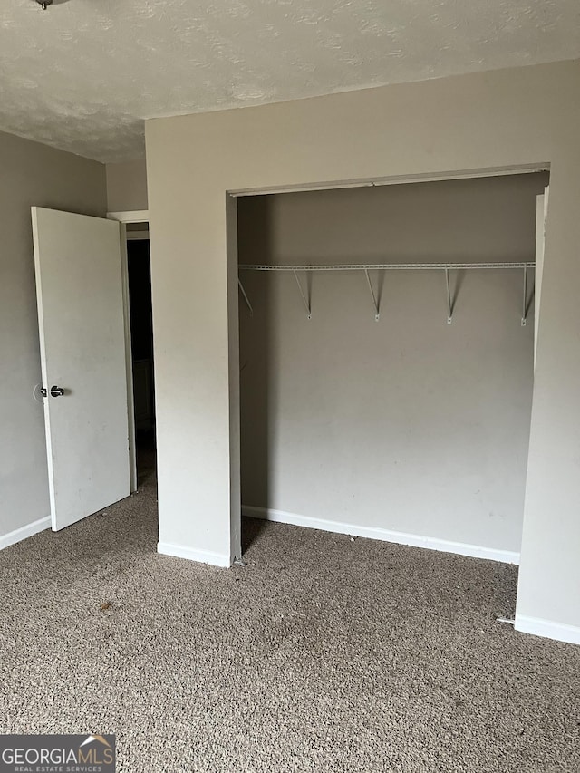 unfurnished bedroom featuring dark colored carpet, a textured ceiling, and a closet