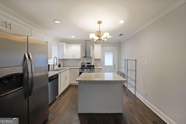 kitchen with appliances with stainless steel finishes, pendant lighting, sink, white cabinets, and wall chimney exhaust hood