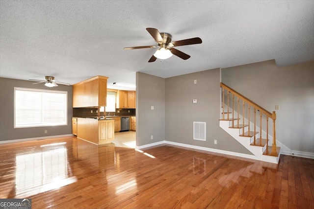 unfurnished living room featuring ceiling fan, sink, a textured ceiling, and light hardwood / wood-style floors