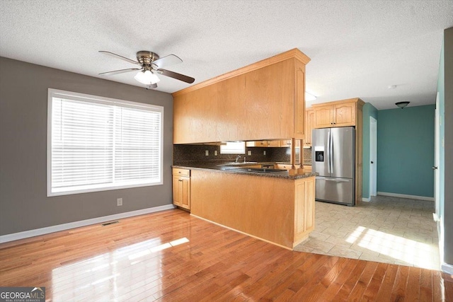 kitchen with ceiling fan, stainless steel refrigerator with ice dispenser, decorative backsplash, kitchen peninsula, and light wood-type flooring