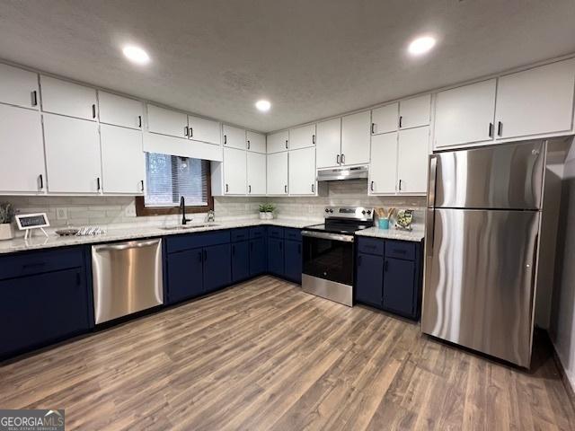 kitchen with appliances with stainless steel finishes, blue cabinets, white cabinetry, sink, and light wood-type flooring