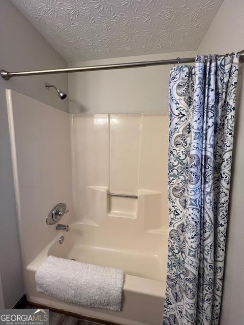 bathroom with shower / bath combination with curtain and a textured ceiling