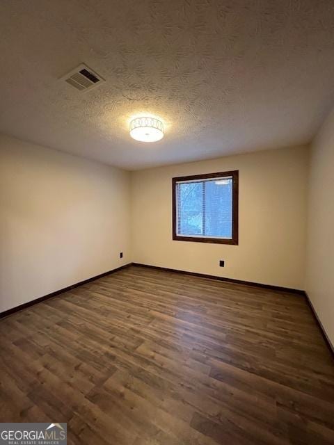 spare room with dark hardwood / wood-style floors and a textured ceiling