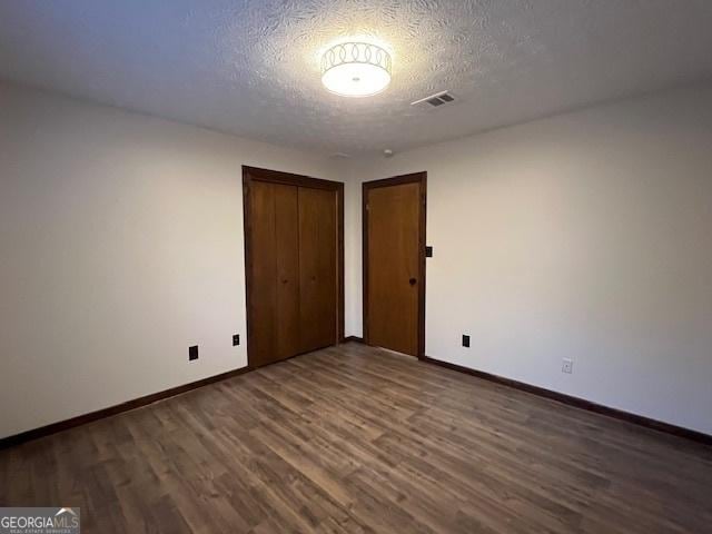 unfurnished bedroom featuring dark wood-type flooring, a textured ceiling, and a closet