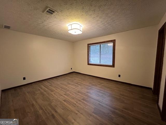 unfurnished room with dark hardwood / wood-style flooring and a textured ceiling