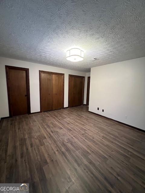 unfurnished bedroom featuring multiple closets, a textured ceiling, and dark hardwood / wood-style flooring