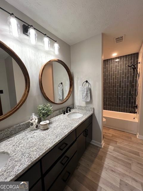 full bathroom with tiled shower / bath, hardwood / wood-style floors, vanity, toilet, and a textured ceiling