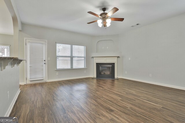 unfurnished living room featuring a fireplace with flush hearth, dark wood finished floors, visible vents, and a ceiling fan