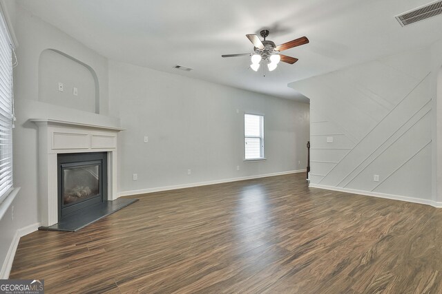 unfurnished living room with dark wood-type flooring, a glass covered fireplace, visible vents, and a ceiling fan