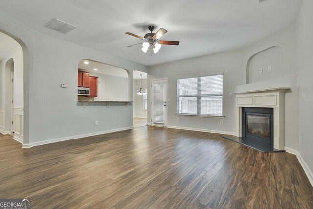 unfurnished living room with visible vents, baseboards, a ceiling fan, dark wood-style floors, and a glass covered fireplace