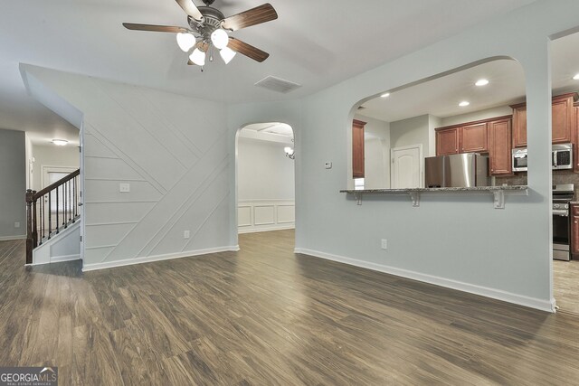 unfurnished living room featuring arched walkways, dark wood-type flooring, visible vents, a ceiling fan, and stairs