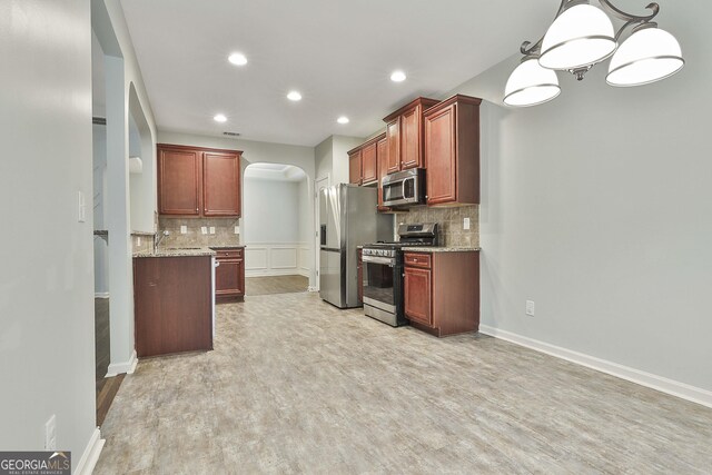 kitchen with light stone counters, arched walkways, pendant lighting, stainless steel appliances, and tasteful backsplash