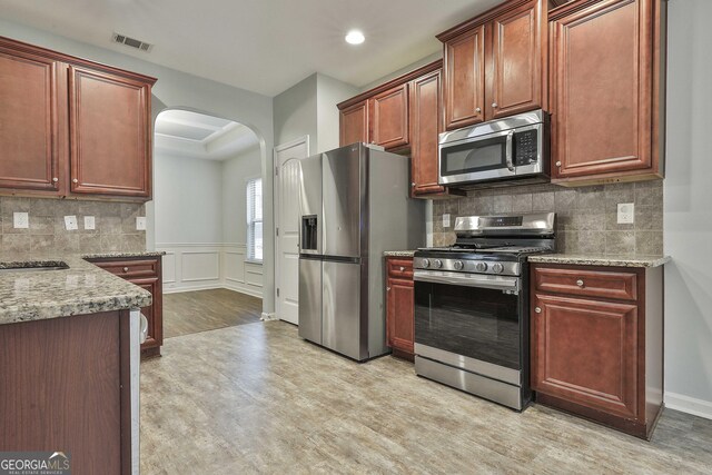 kitchen with light stone counters, arched walkways, stainless steel appliances, visible vents, and decorative backsplash