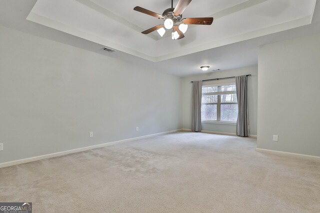 spare room with a raised ceiling, light colored carpet, visible vents, a ceiling fan, and baseboards