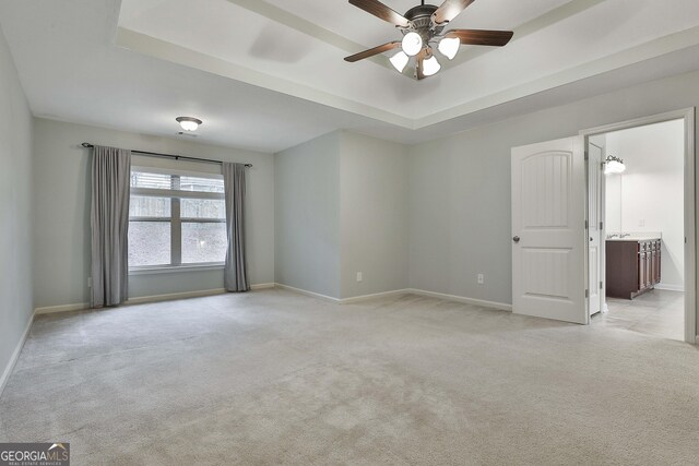 empty room with a ceiling fan, a tray ceiling, light colored carpet, and baseboards