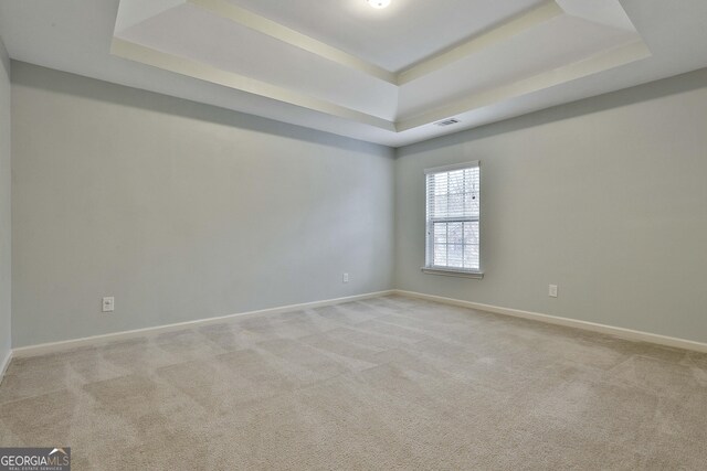 spare room featuring a raised ceiling, light carpet, and baseboards