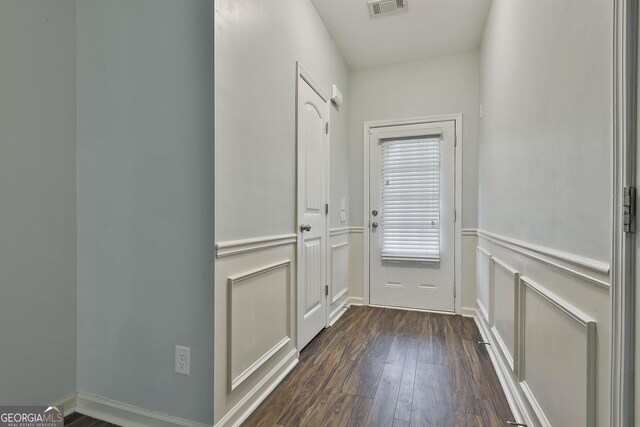 doorway to outside featuring visible vents, wainscoting, dark wood finished floors, and a decorative wall