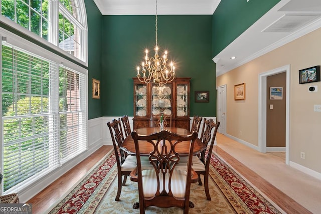 dining space with crown molding, light hardwood / wood-style floors, an inviting chandelier, and a high ceiling