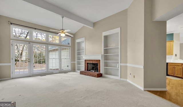 unfurnished living room featuring beamed ceiling, light colored carpet, ceiling fan, a brick fireplace, and built in shelves