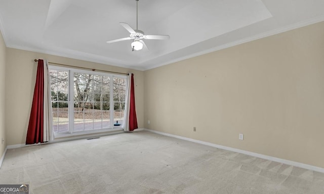 empty room with a raised ceiling, ornamental molding, light carpet, and ceiling fan