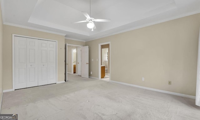 unfurnished bedroom with crown molding, connected bathroom, a tray ceiling, light colored carpet, and a closet