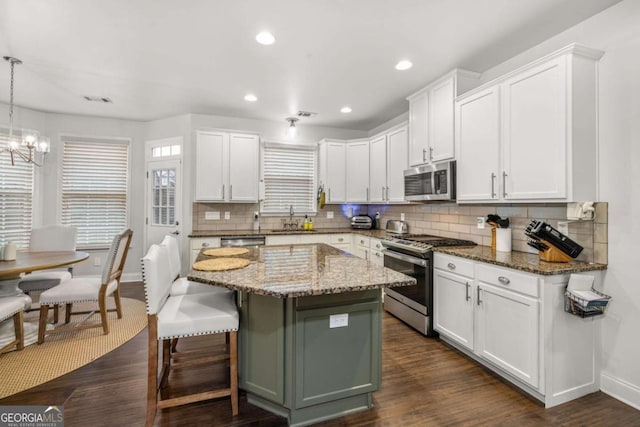 kitchen with stainless steel appliances, a kitchen island, a sink, white cabinets, and pendant lighting